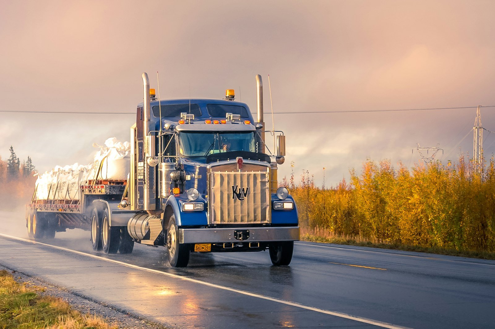 Blue Kenworth semi-truck hauling a flatbed load, serviced by Quality Truck Repair Inc. in Bloomington, CA